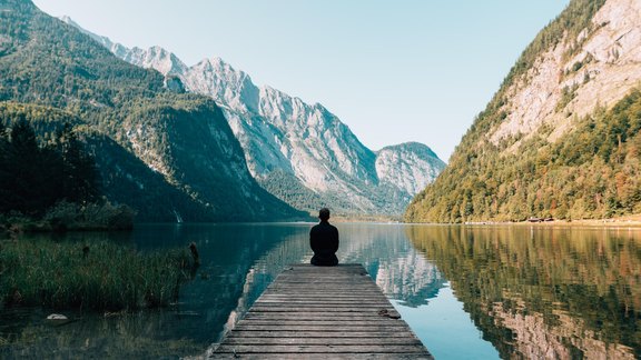 Reisender sitzt auf Steg an Bergsee - Foto: Migaj/unsplash